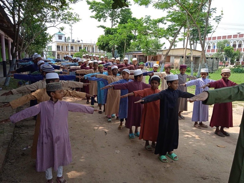 Boys standing in rows with arms outstretched during morning exercise outdoors